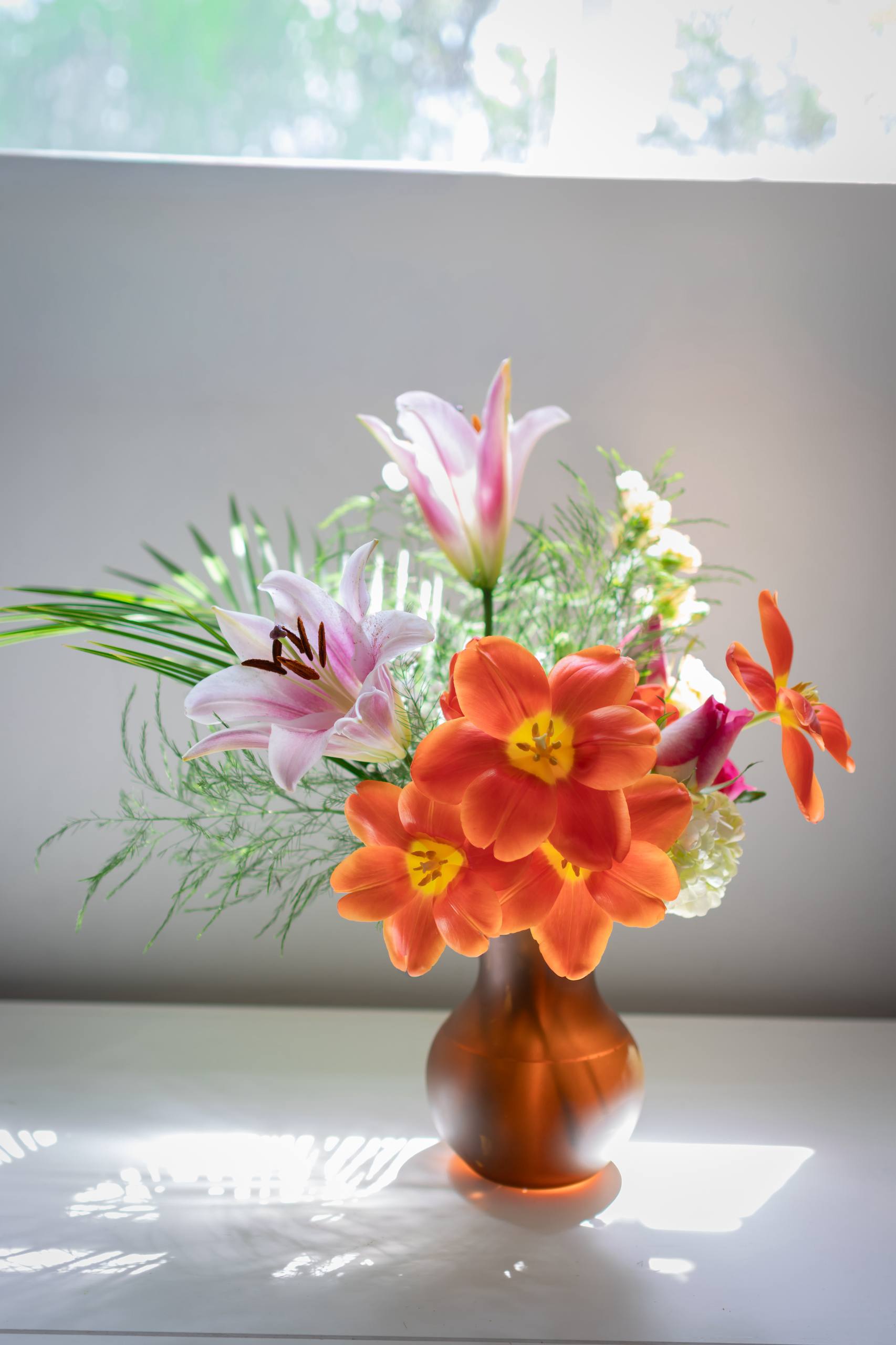 Vibrant floral arrangement with orange blossoms and pink lilies in a bronze vase